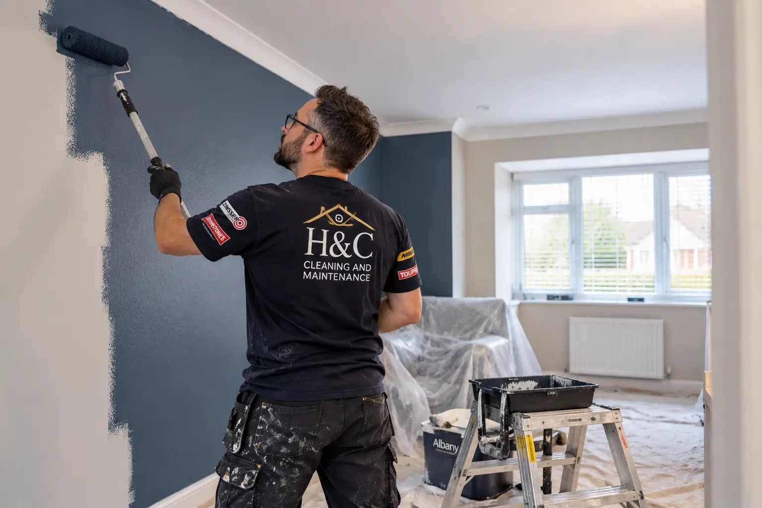 Matt roller painting a dark grey feature wall in a Hailsham home